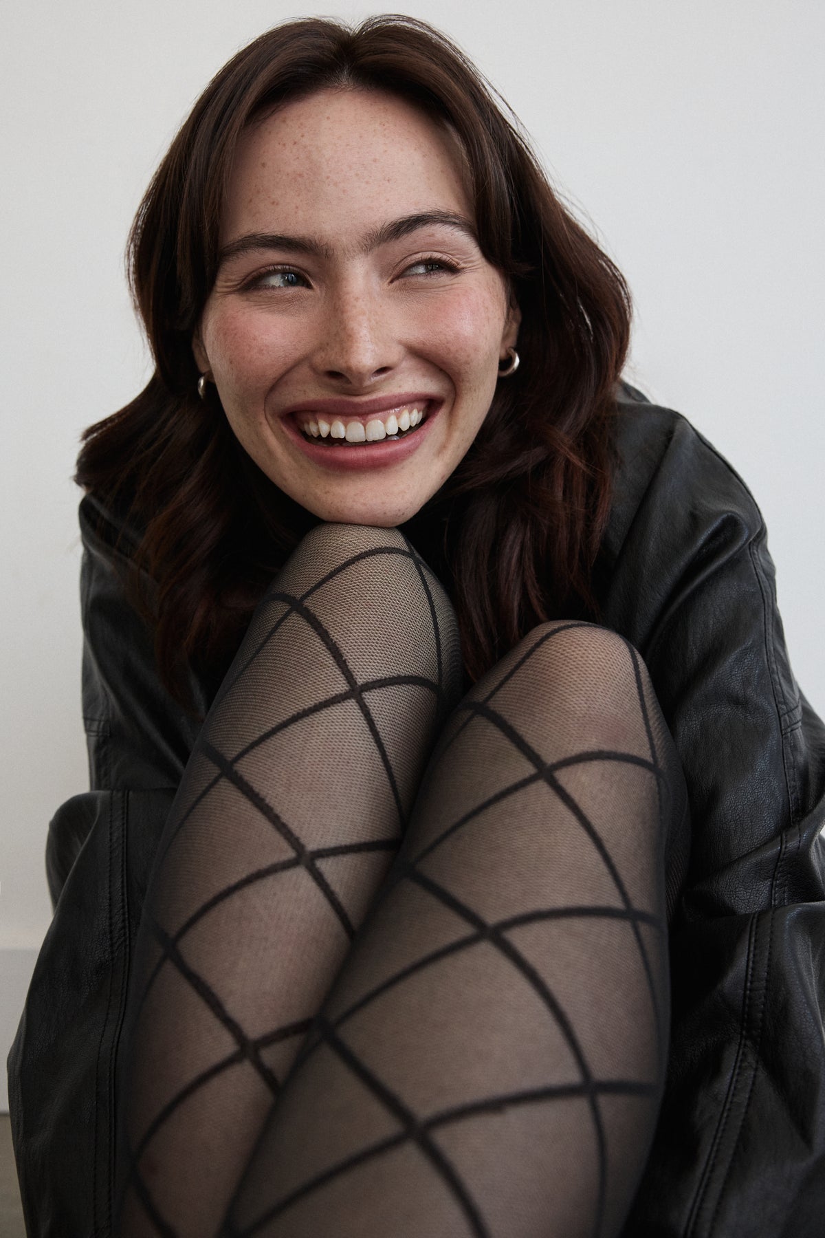 A model laughing, wearing the Large Argyle Tights in Black with a black top.