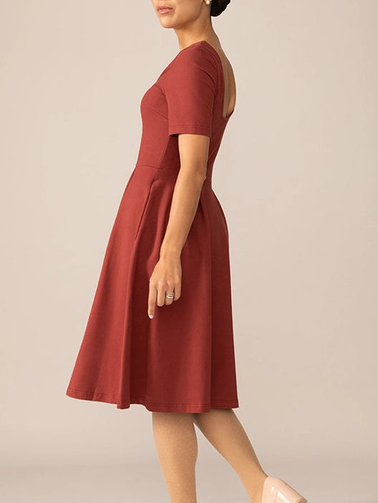 A woman wearing a red short sleeve ballerina knit dress with a fit-and-flare design, standing on tiptoe, facing away from the camera.