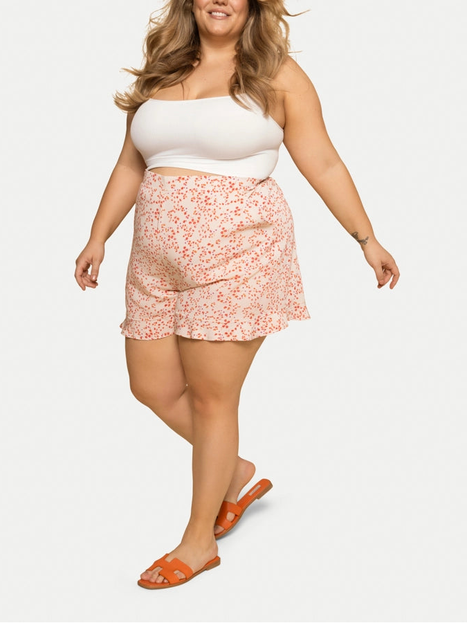A close-up of a woman's knee-length beige shorts with a floral pattern and a ruffled hemline.
